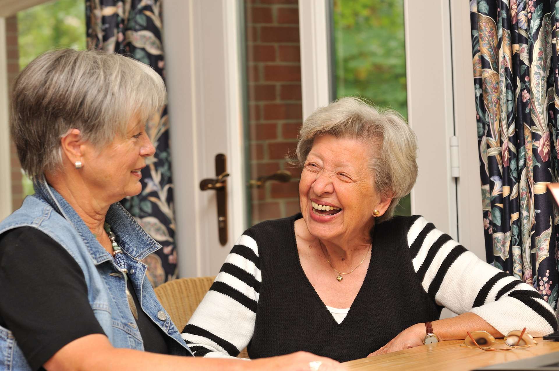 Zwei ältere Damen unterhalten sich lachend an einem Tisch.