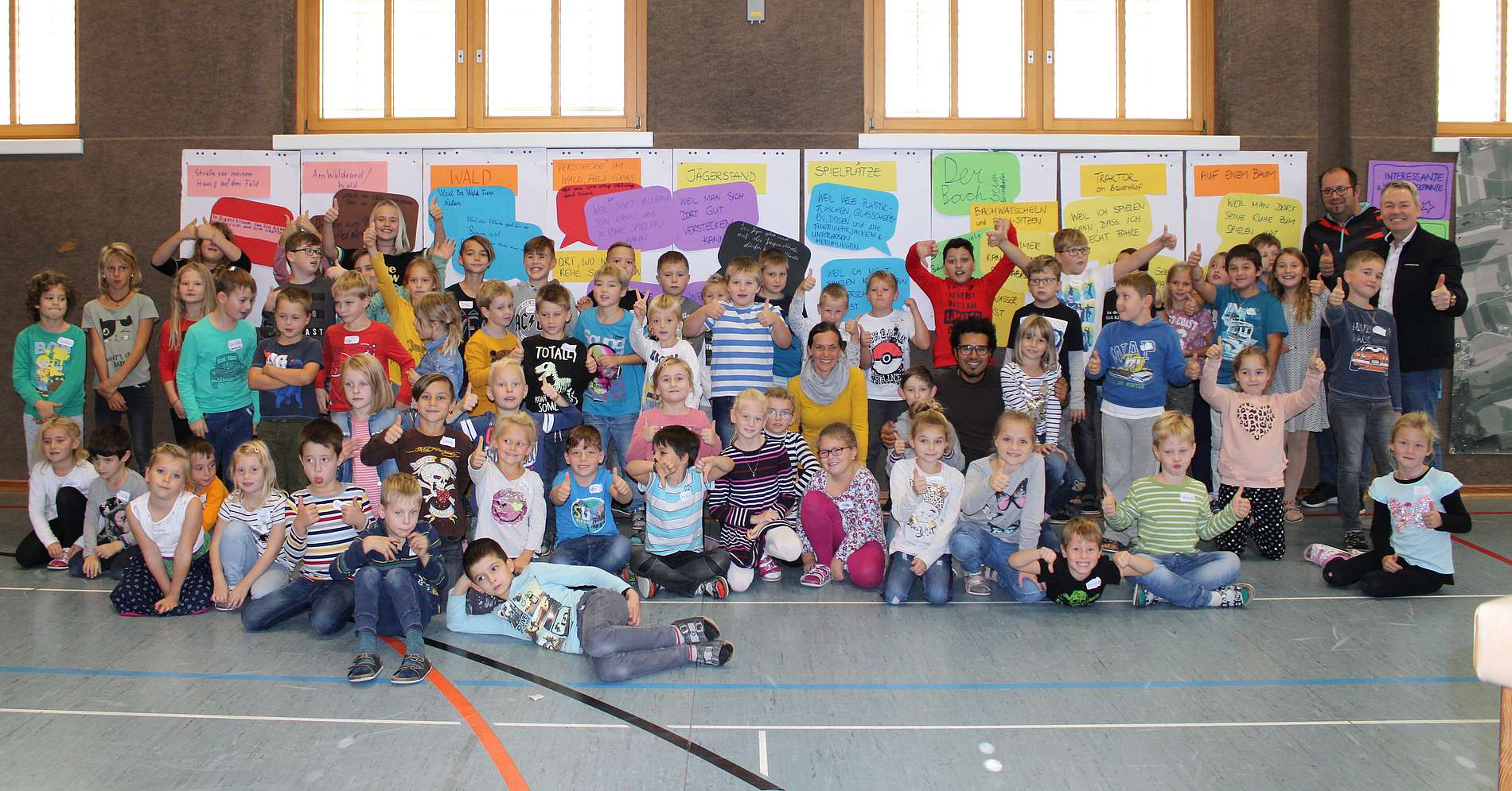 50 Kinder präsentieren ihre ausgearbeiten Plakate in einem Turnsaal