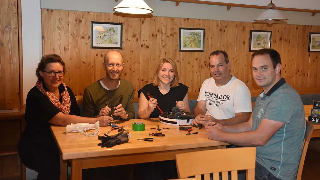 5 Personen an einem Tisch, reparieren Geräte