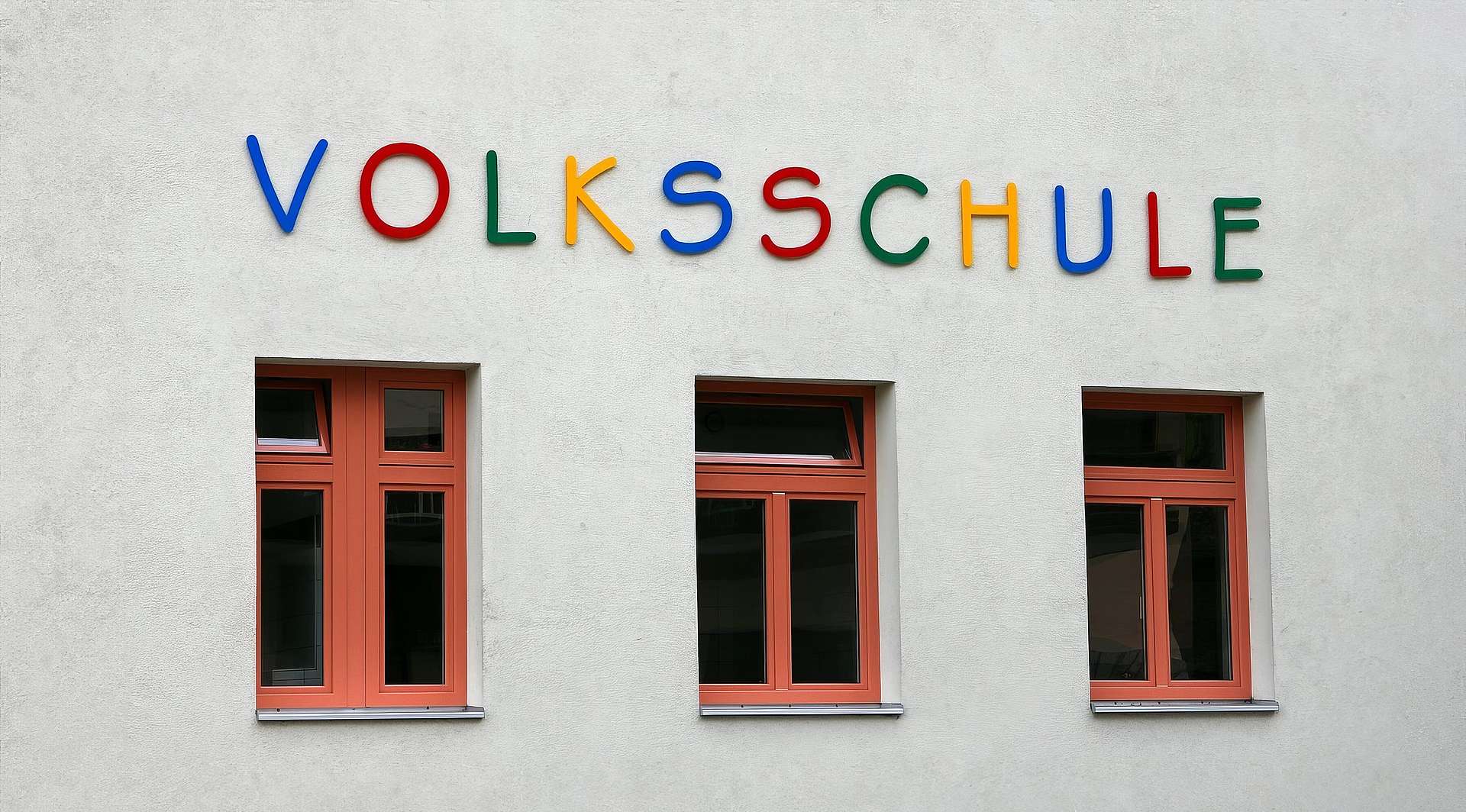 Fassade mit drei Fenstern und der bunten Aufschrift "Volksschule"