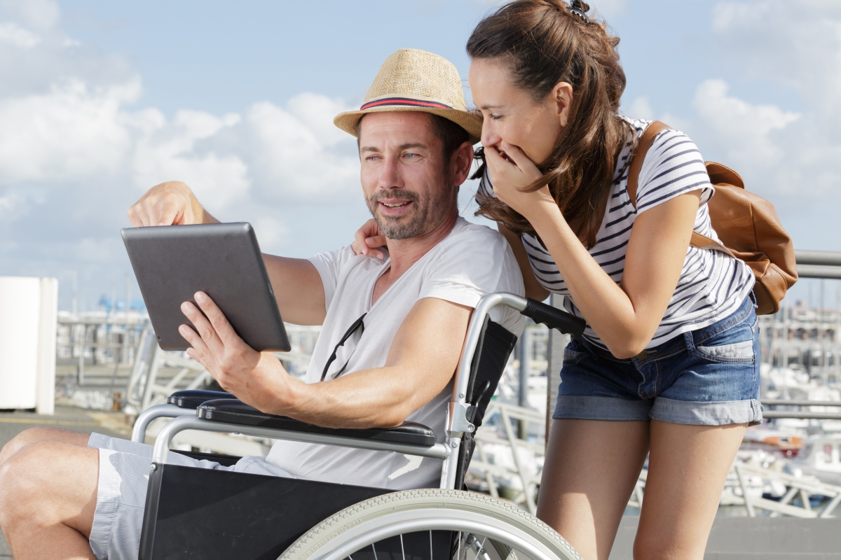 Mann im Rollstuhl und eine Frau blicken auf ein Tablet - als Symbol für digitale Barrierefreiheit 